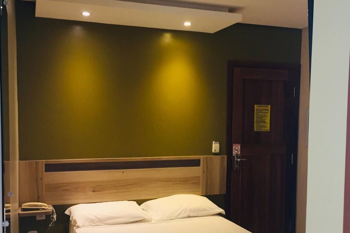 A hotel room with a single bed, a wooden headboard, a bedside telephone, and a door with a sign.