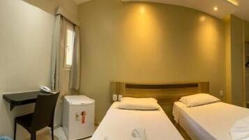 Habitación de hotel con dos camas, un escritorio, una silla, una mesita y un baño visible al fondo.
