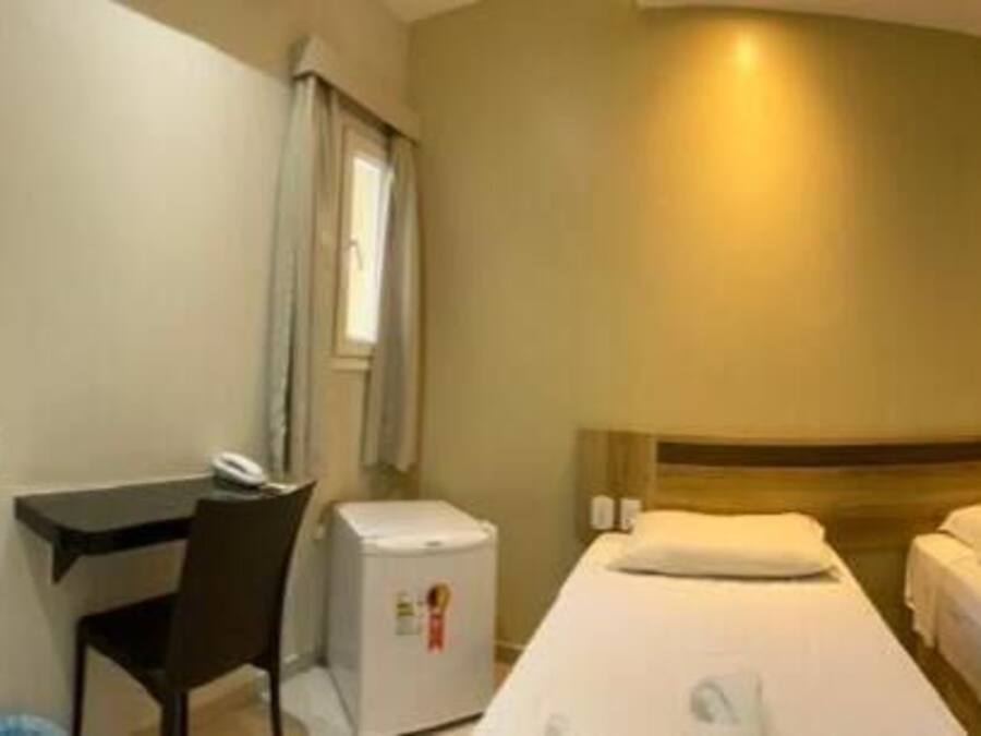 Habitación de hotel con dos camas, un escritorio, una silla, una mesita y un baño visible al fondo.