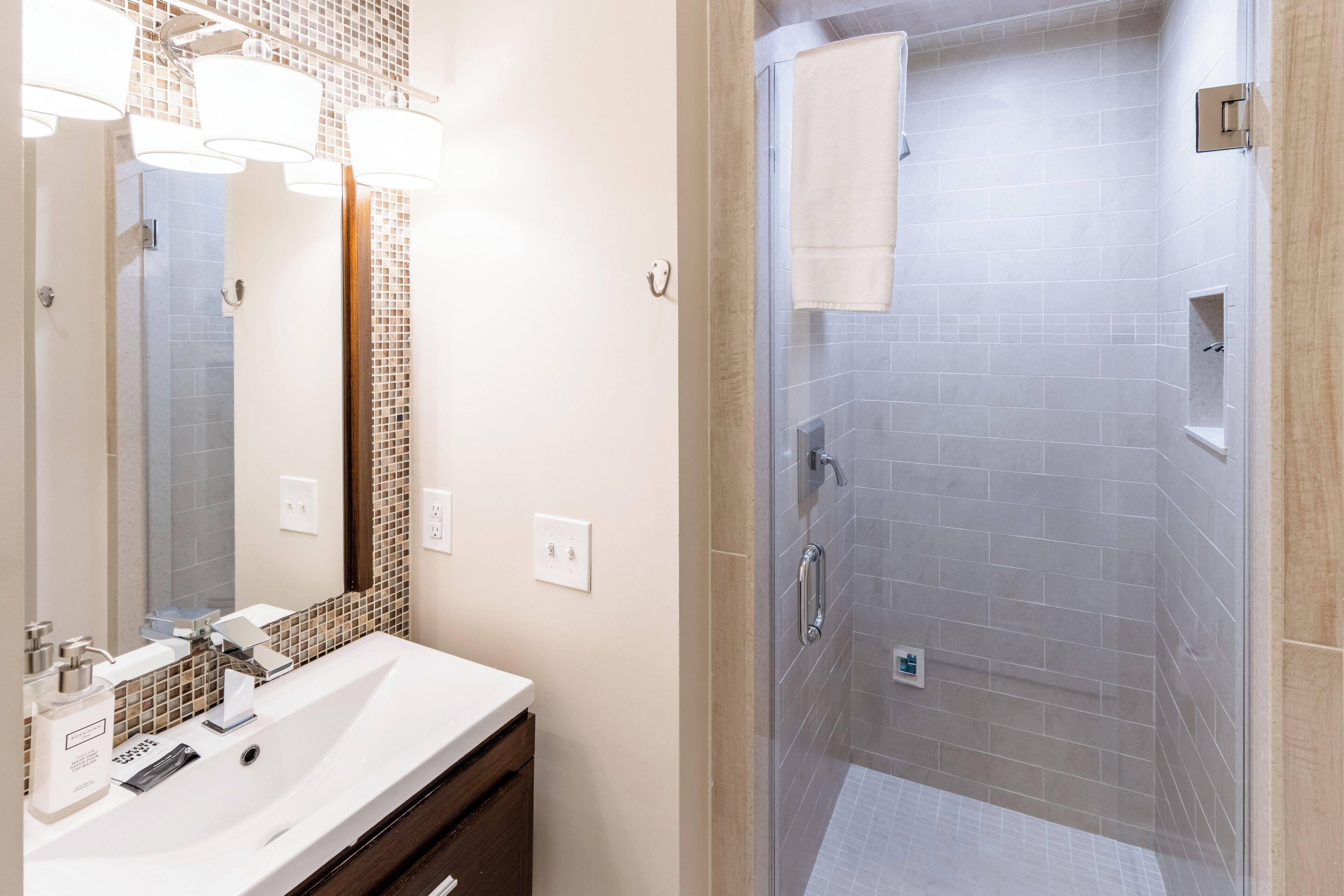 Une salle de bain moderne avec un grand miroir, un lavabo avec un meuble-vasque et une douche à l’italienne.