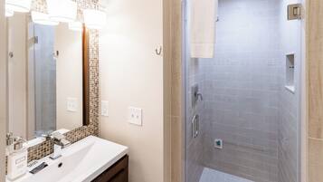 Une salle de bain moderne avec un grand miroir, un lavabo avec un meuble-vasque et une douche à l’italienne.