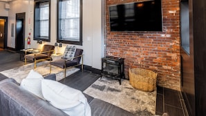 Een moderne woonkamer met een bakstenen muur, een flatscreen-televisie, een bank, een fauteuil en een open haard.