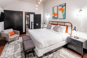 A modern bedroom with a large bed, bedside tables, a chair, and a desk. - The Firehouse (Newport)