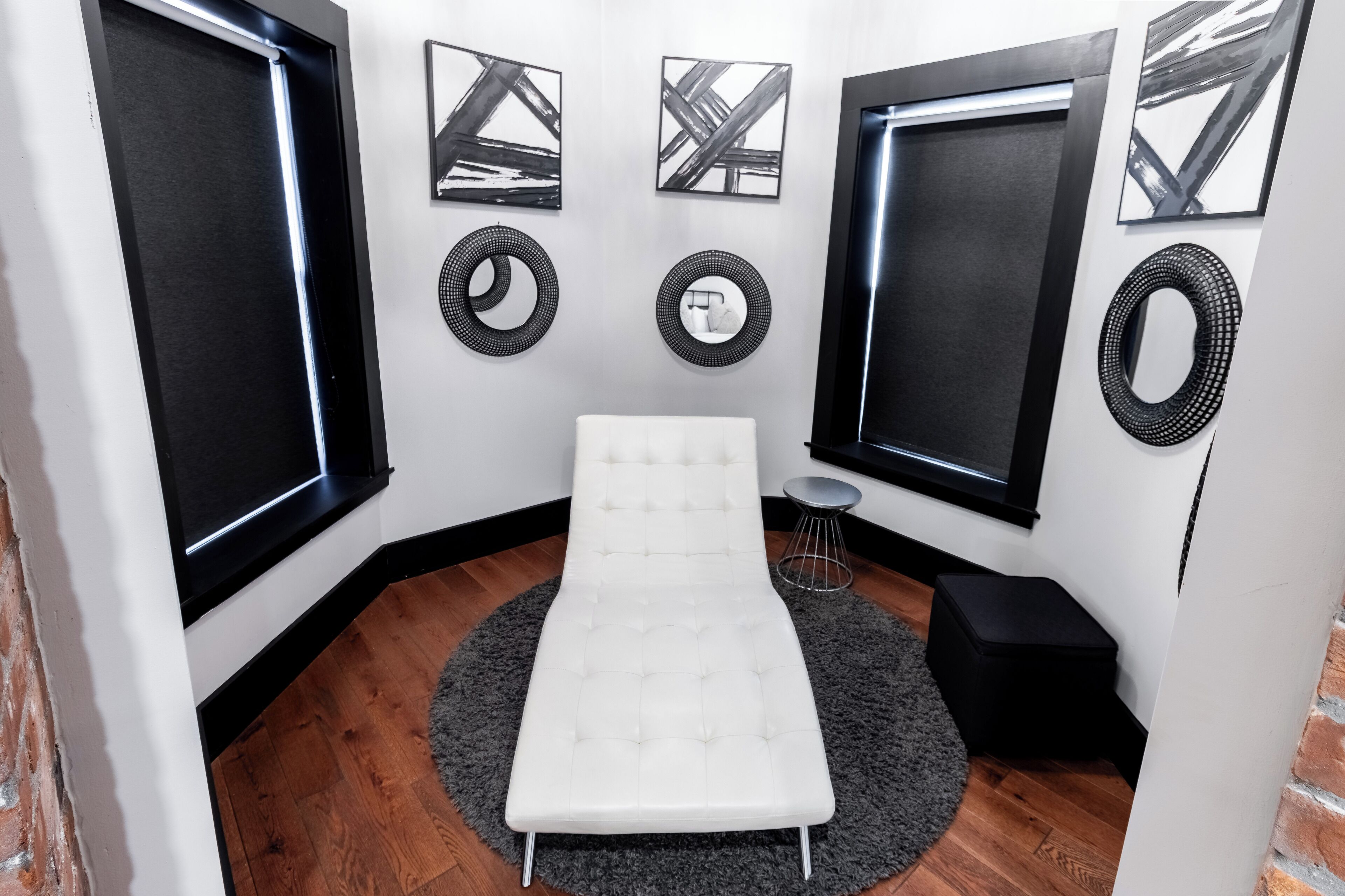 Ein Zimmer mit einer weißen gepolsterten Bank, einem runden Teppich und einem kleinen Hocker. An den Wänden hängen drei gerahmte Kunstwerke und zwei runde Wanddekorationen.