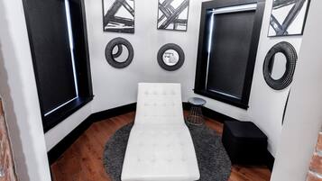 Ein Zimmer mit einer weißen gepolsterten Bank, einem runden Teppich und einem kleinen Hocker. An den Wänden hängen drei gerahmte Kunstwerke und zwei runde Wanddekorationen.