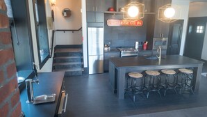 Een moderne keuken met een centraal eiland, barstoelen, roestvrijstalen apparatuur en hanglampen.