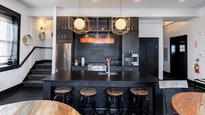 Een moderne keuken met een centraal eiland, barkrukken en een neonbord.