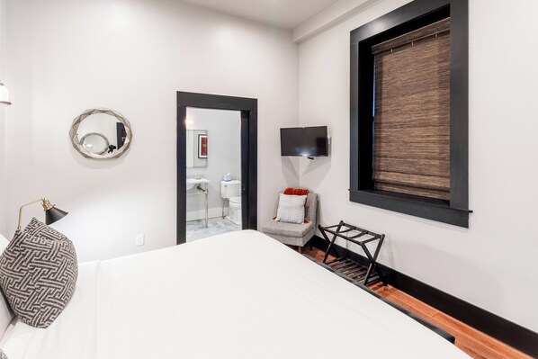 A modern hotel room with a large bed, a round mirror, a television, and a chair.
