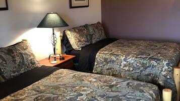 A room with two beds, a nightstand, a lamp, and a framed picture on the wall.