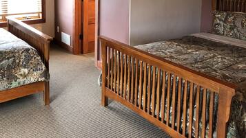 A bedroom with two beds, a wooden ceiling, a wall-mounted light fixture, and a door leading to another room.