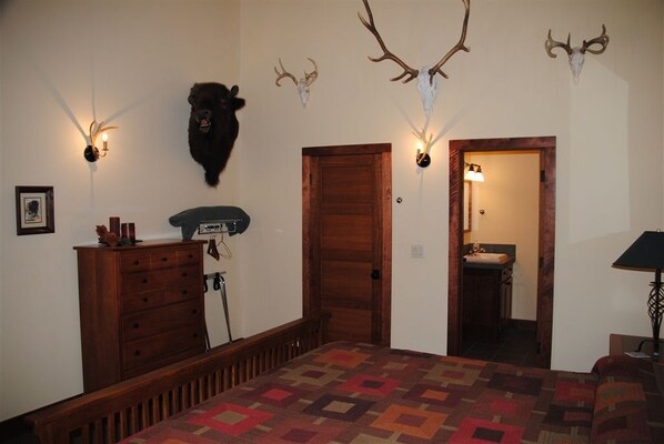 A bedroom with a patterned carpet, wooden dresser, and a door leading to a bathroom. - ReWild Ranch (Sargent)