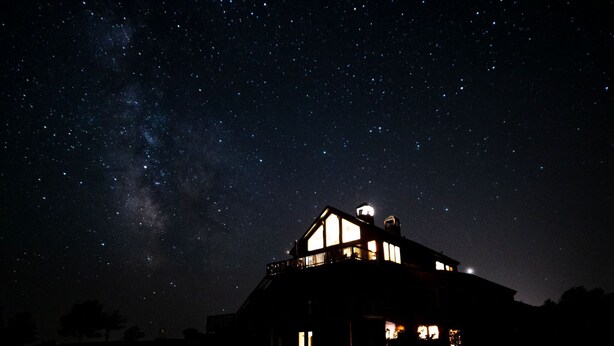 A house with a dark sky background and visible stars, including the Milky Way.
