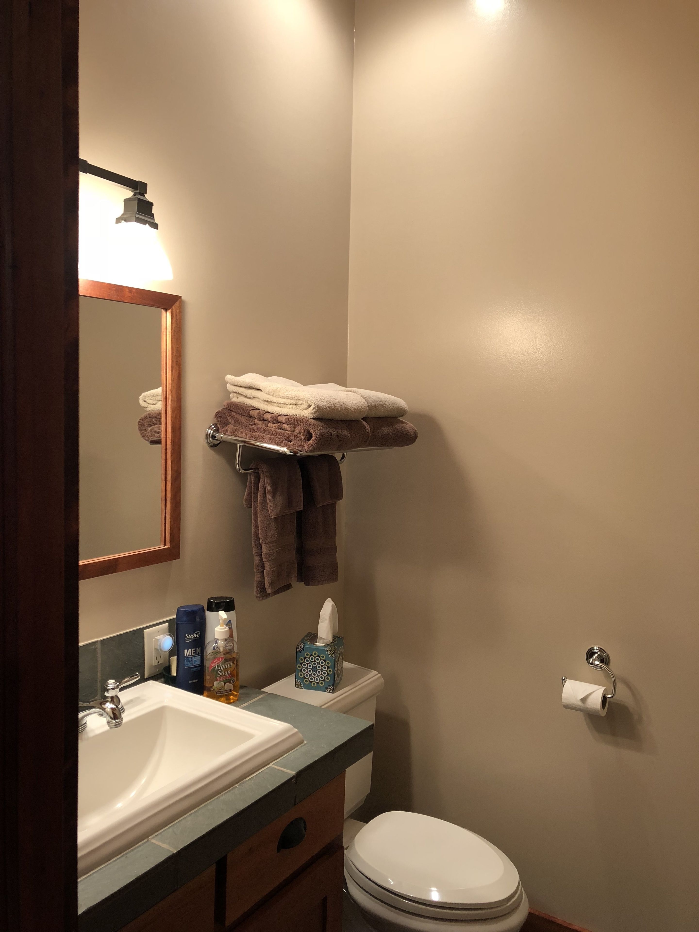A bathroom with a sink, mirror, towel rack, toilet, and a bottle of liquid soap.