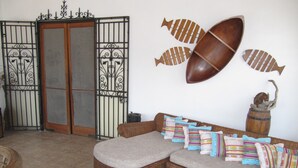 A living room with a wicker sofa, colorful pillows, a wooden fish wall art, a rustic barrel, and a metal gate. - Casa Playas 1 (Playas)