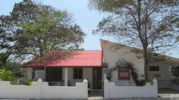 A two-story building with a red roof and white walls, featuring a gated entrance and a signboard.
