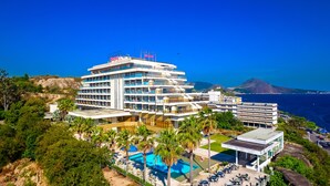 A multi-story hotel with a pool area and outdoor seating, surrounded by greenery and overlooking a coastal landscape.
