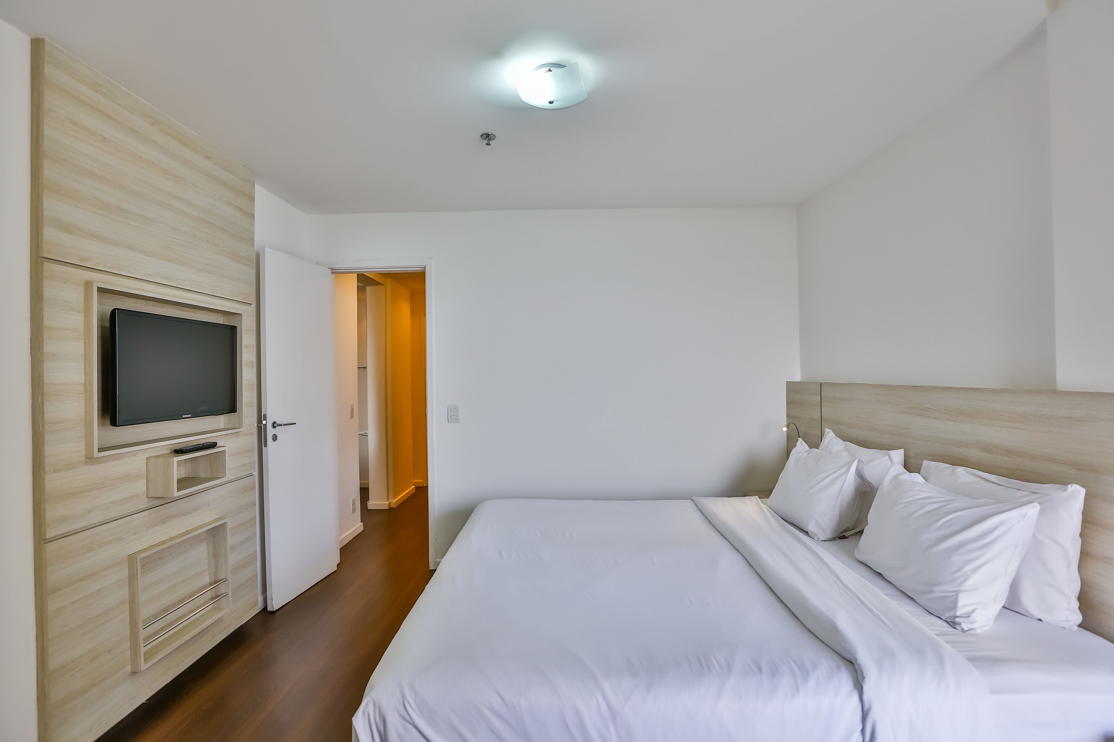 Een hotelkamer met een bed, een televisie op een houten kast en een deur die naar een andere kamer leidt.