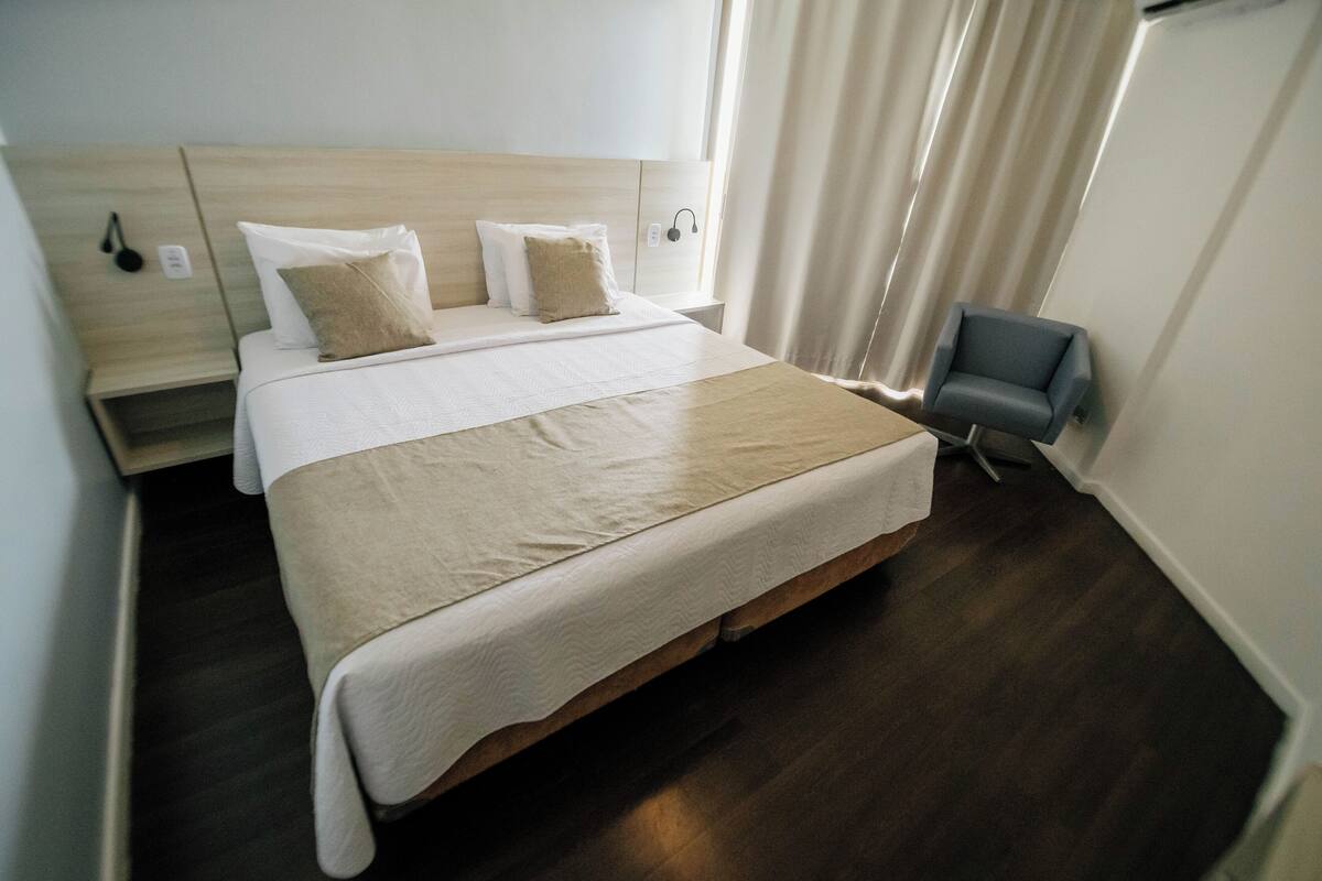 A neatly made bed with a wooden headboard, a bedside table with a lamp, and a chair.