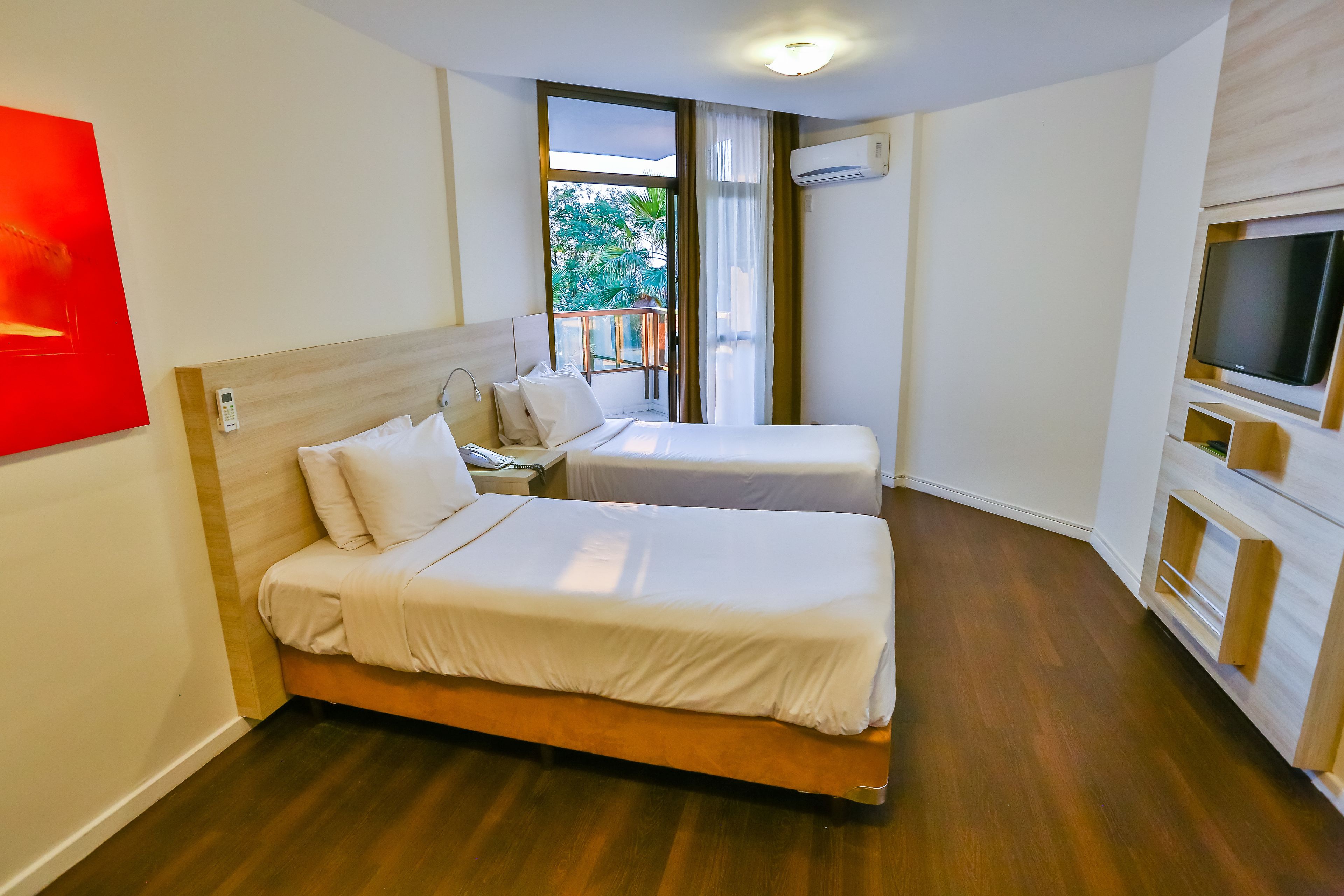 Ein Hotelzimmer mit zwei Betten, einem Fernseher und einem Balkon mit Blick auf Bäume.