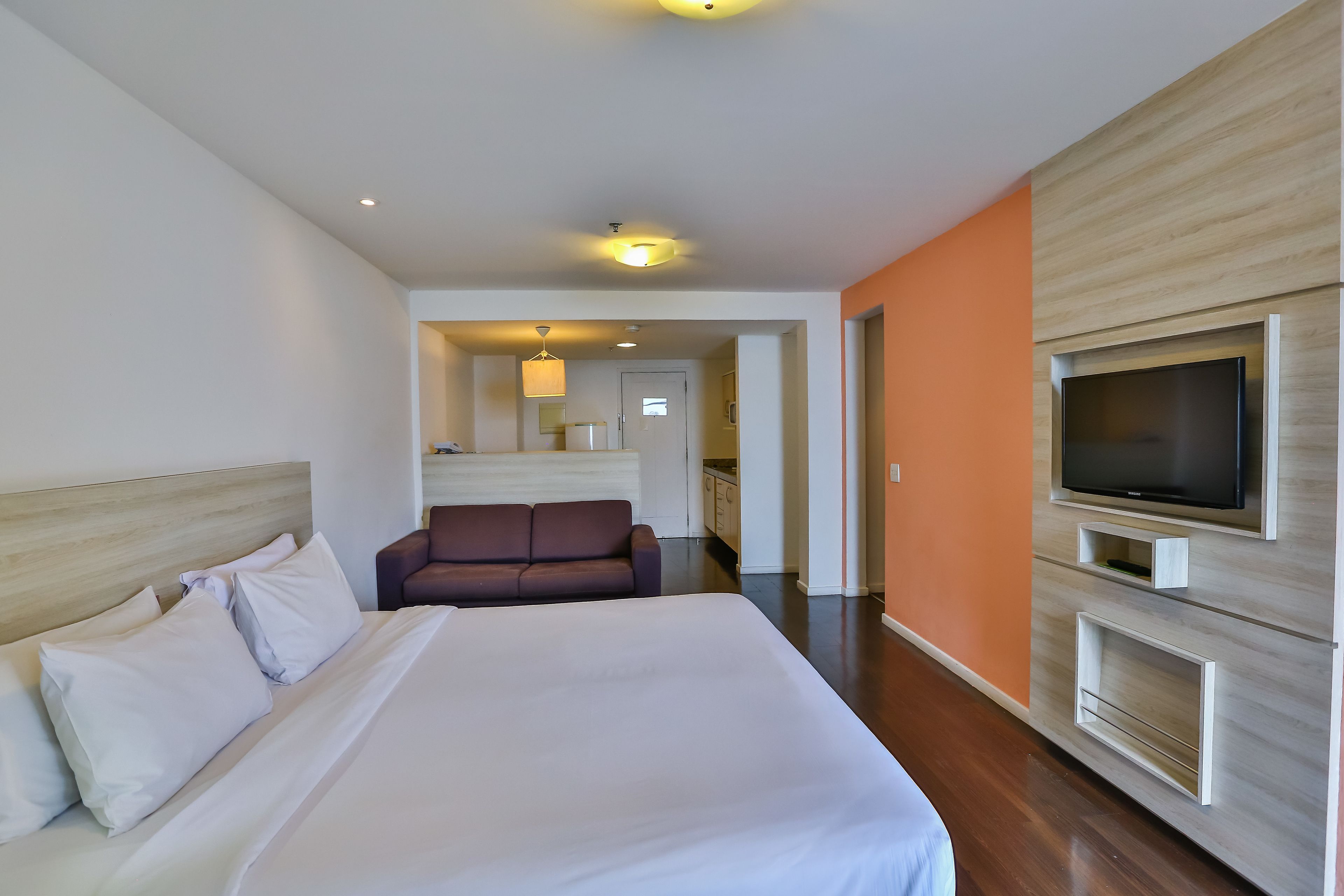 A hotel room with a large bed, a television mounted on the wall, and a sofa in the background.