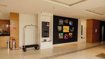 Un vestíbulo de hotel con un diseño moderno y limpio, que presenta un muro con ilustraciones coloridas, un extintor, un carrito y un cartel que indica la ubicación.