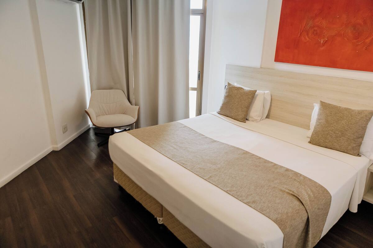A hotel room with a large bed, a chair, and a window with curtains.