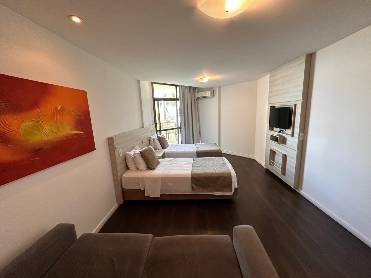 Una habitación de hotel moderna con una cama grande, un sofá, un televisor y un cuadro en la pared.