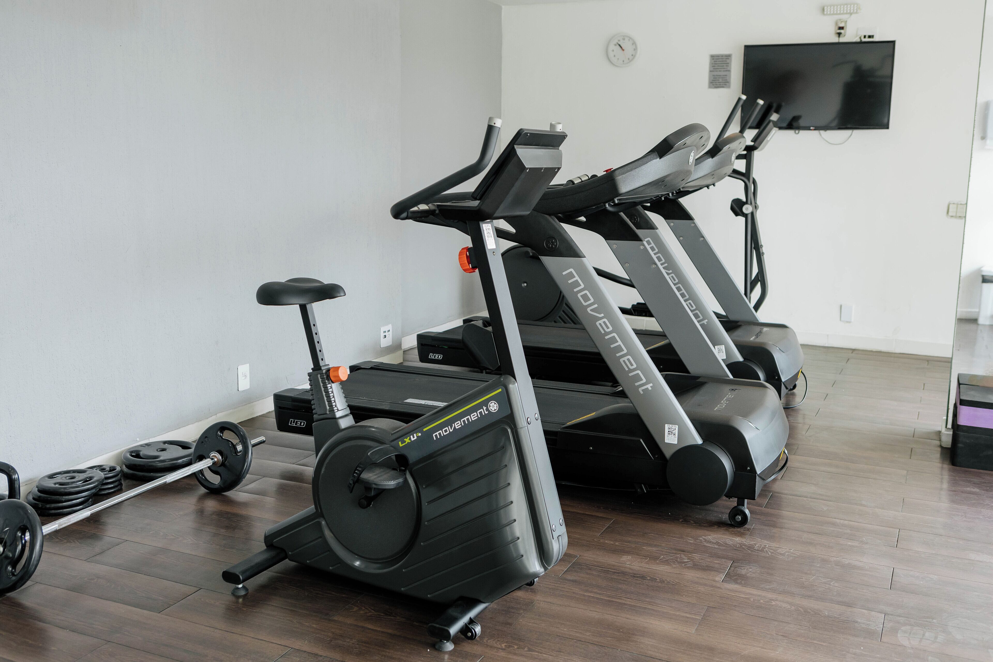 A home gym with two treadmills, a stationary bike, and a set of weights.