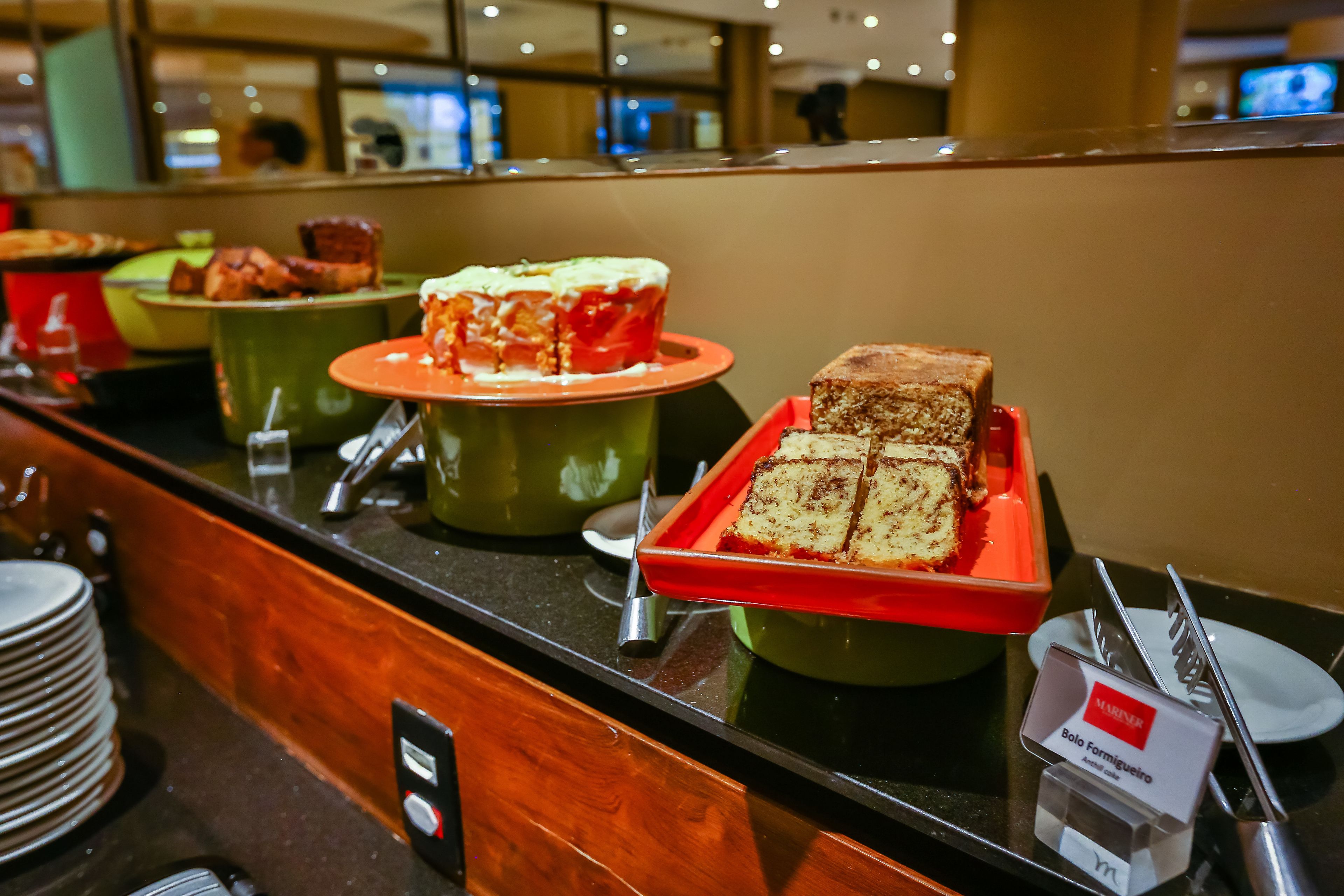A buffet counter with various food items, including a cake and a loaf of bread, in green and red serving dishes.