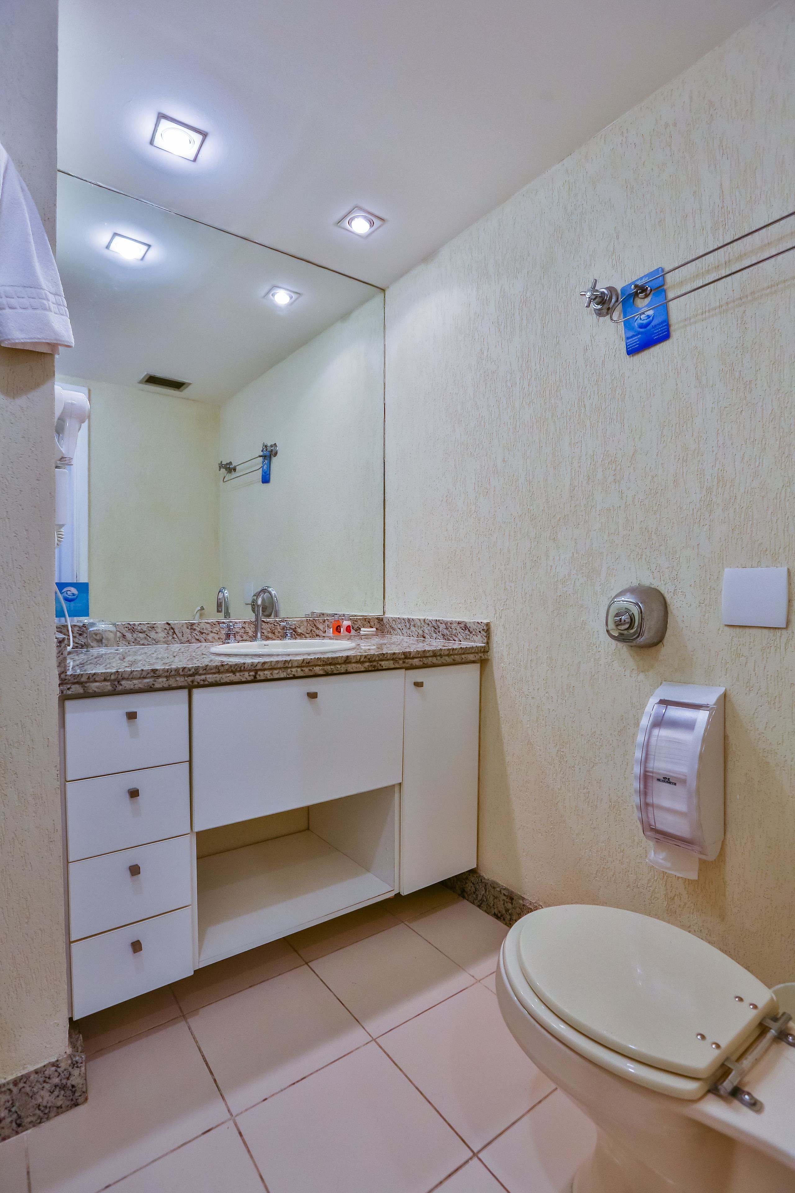 A bathroom with a sink, mirror, towel dispenser, and toilet.