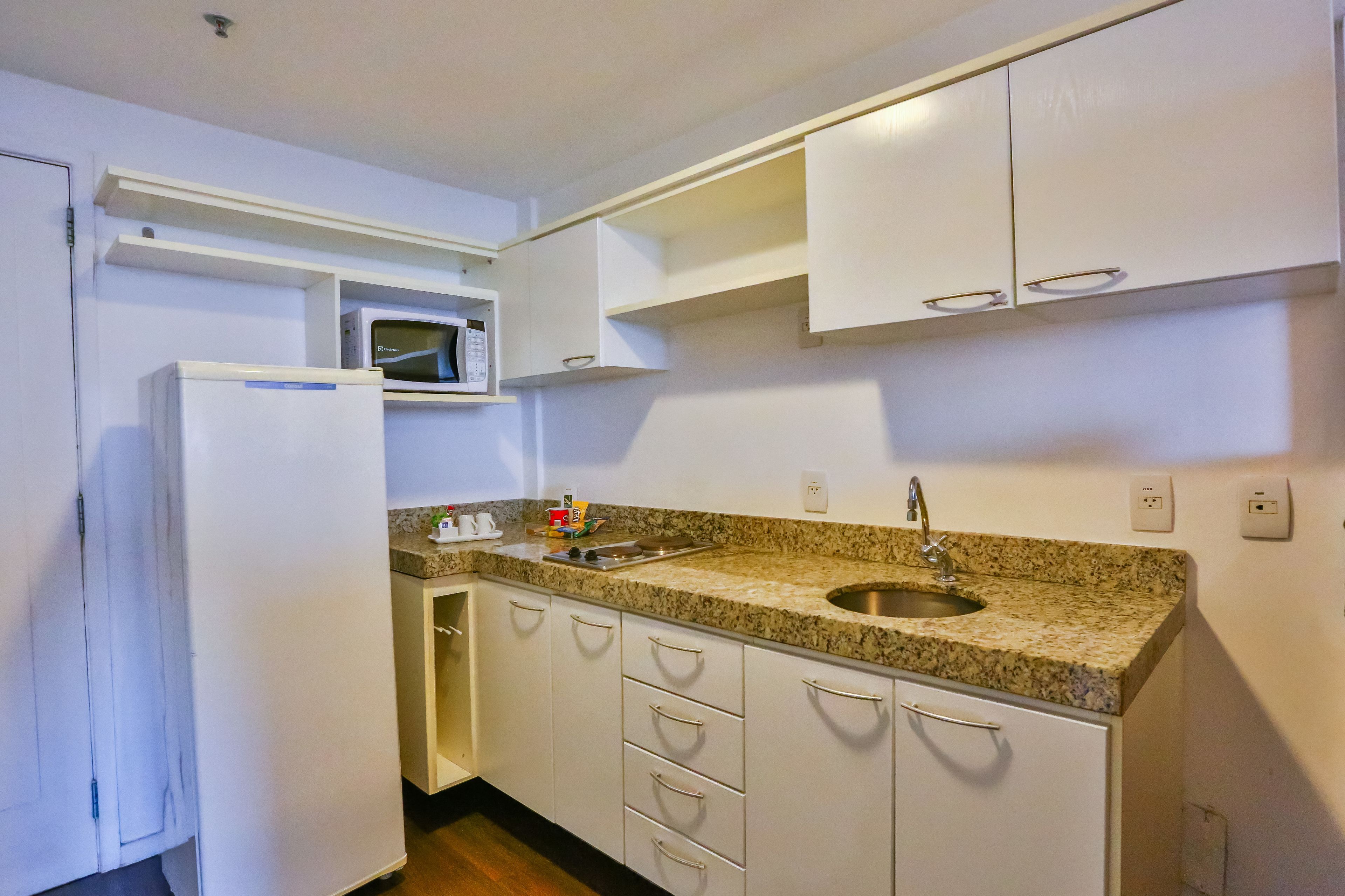 A compact kitchen with white cabinets, a built-in microwave, a granite countertop, and a sink.