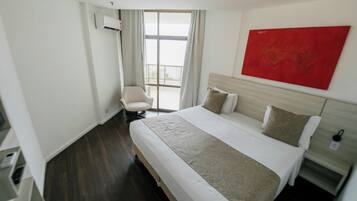 A hotel room with a large bed, a chair, a red artwork on the wall, and a window with curtains.
