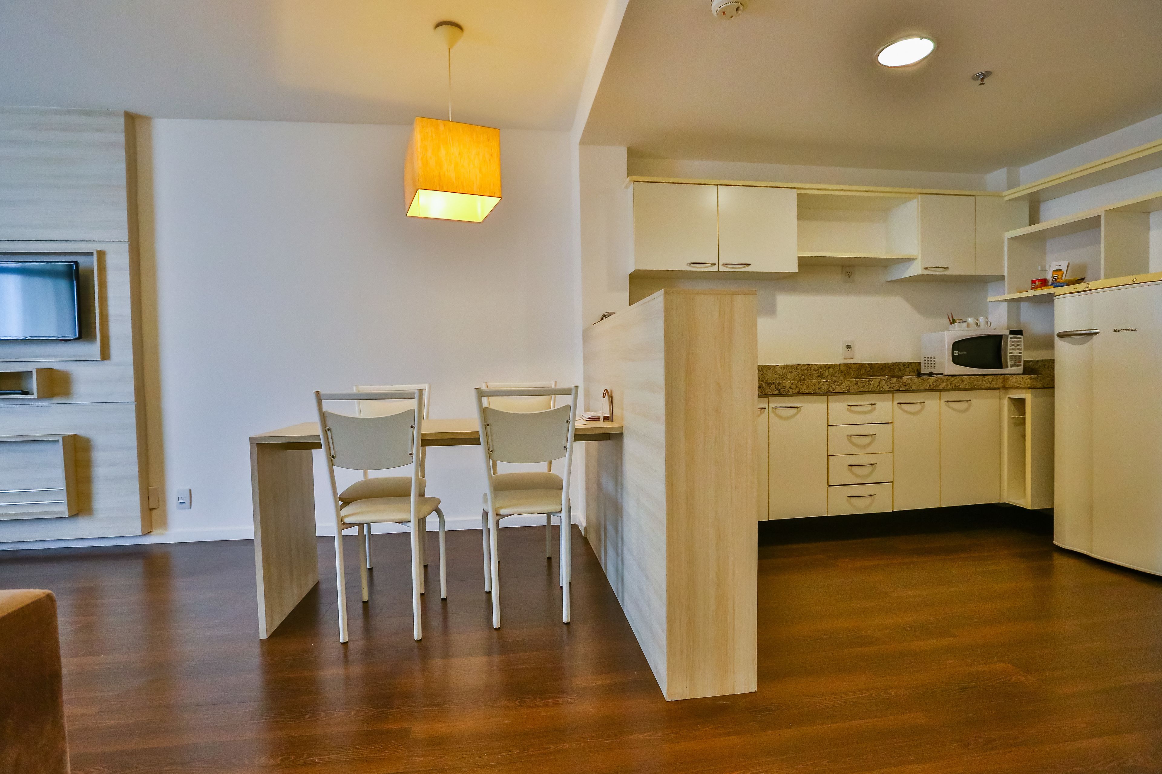 A modern kitchen with white cabinets, a wooden dining table with chairs, a microwave, and a pendant light.