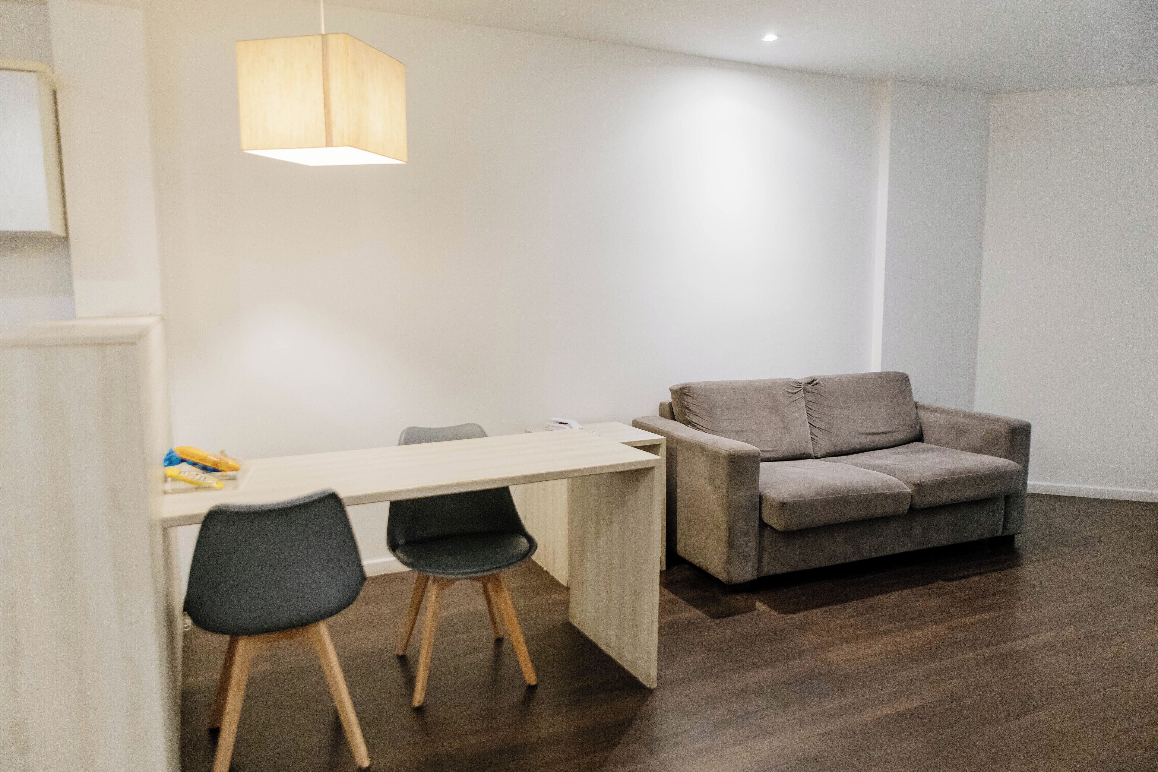 Una sala de estar moderna con una mesa de comedor de madera, dos sillas negras, un sofá gris y una lámpara colgante.