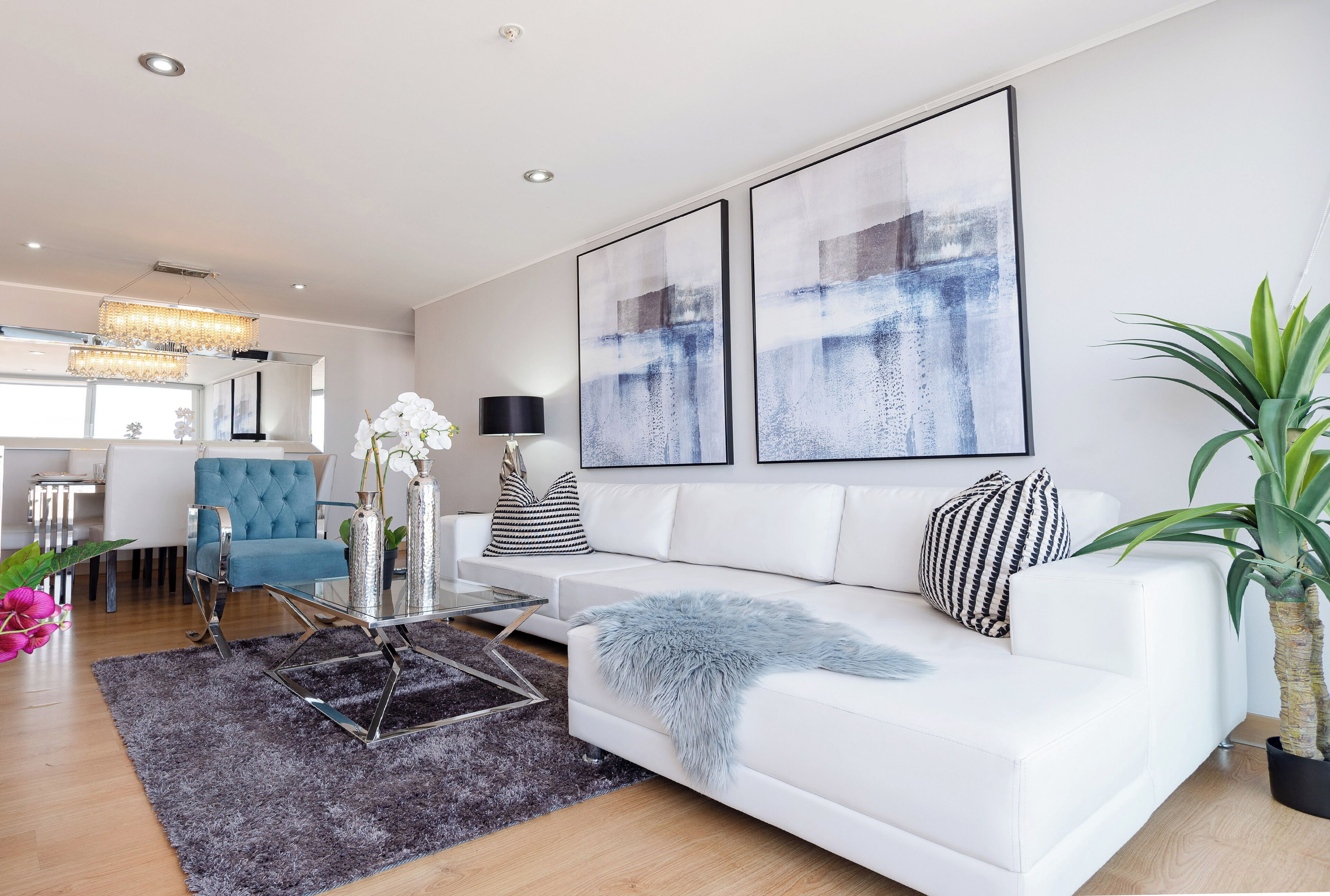 A modern living room with a white sofa, a glass coffee table, and abstract art on the wall.