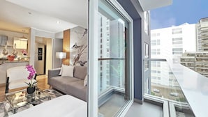 Un appartement moderne doté d’un balcon en verre, d’un salon avec un canapé et une table basse, et d’un coin cuisine comprenant un réfrigérateur et une table à manger.