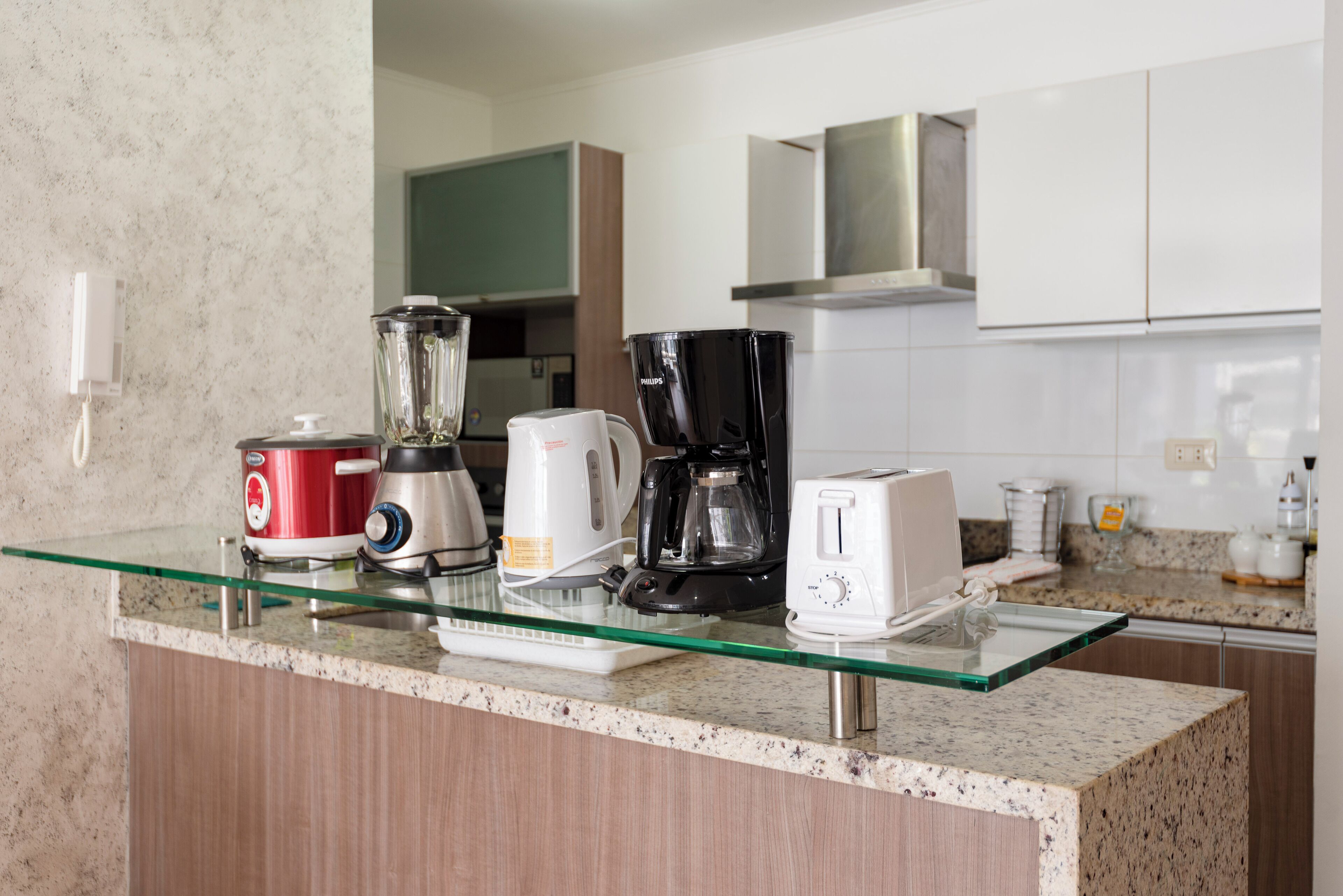 A kitchen counter with a blender, coffee maker, toaster, and a glass coffee pot.