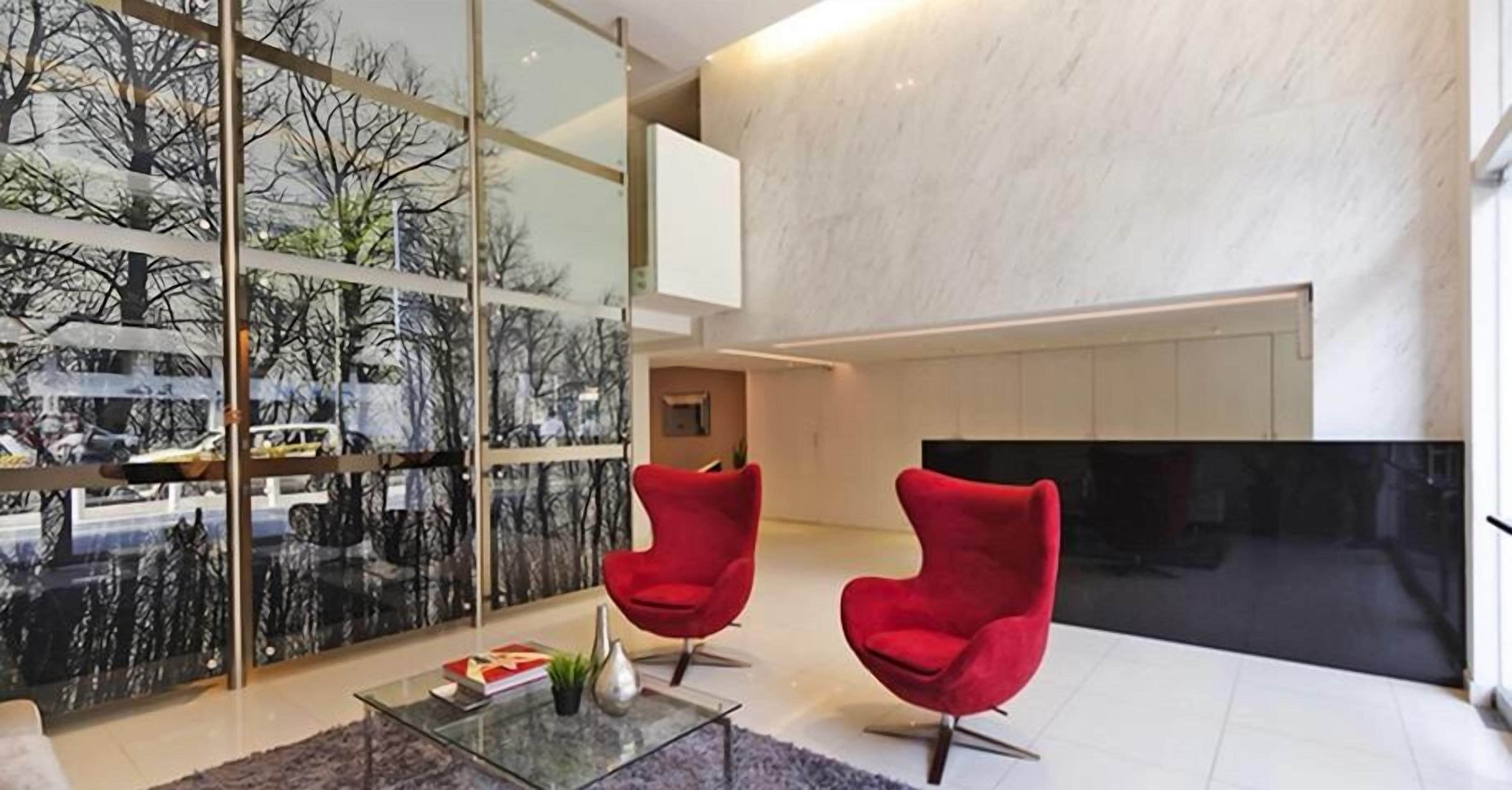 A modern living room with two red chairs, a glass coffee table, and a large TV.