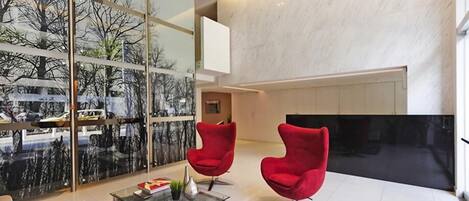 A modern living room with two red chairs, a glass coffee table, and a large TV.