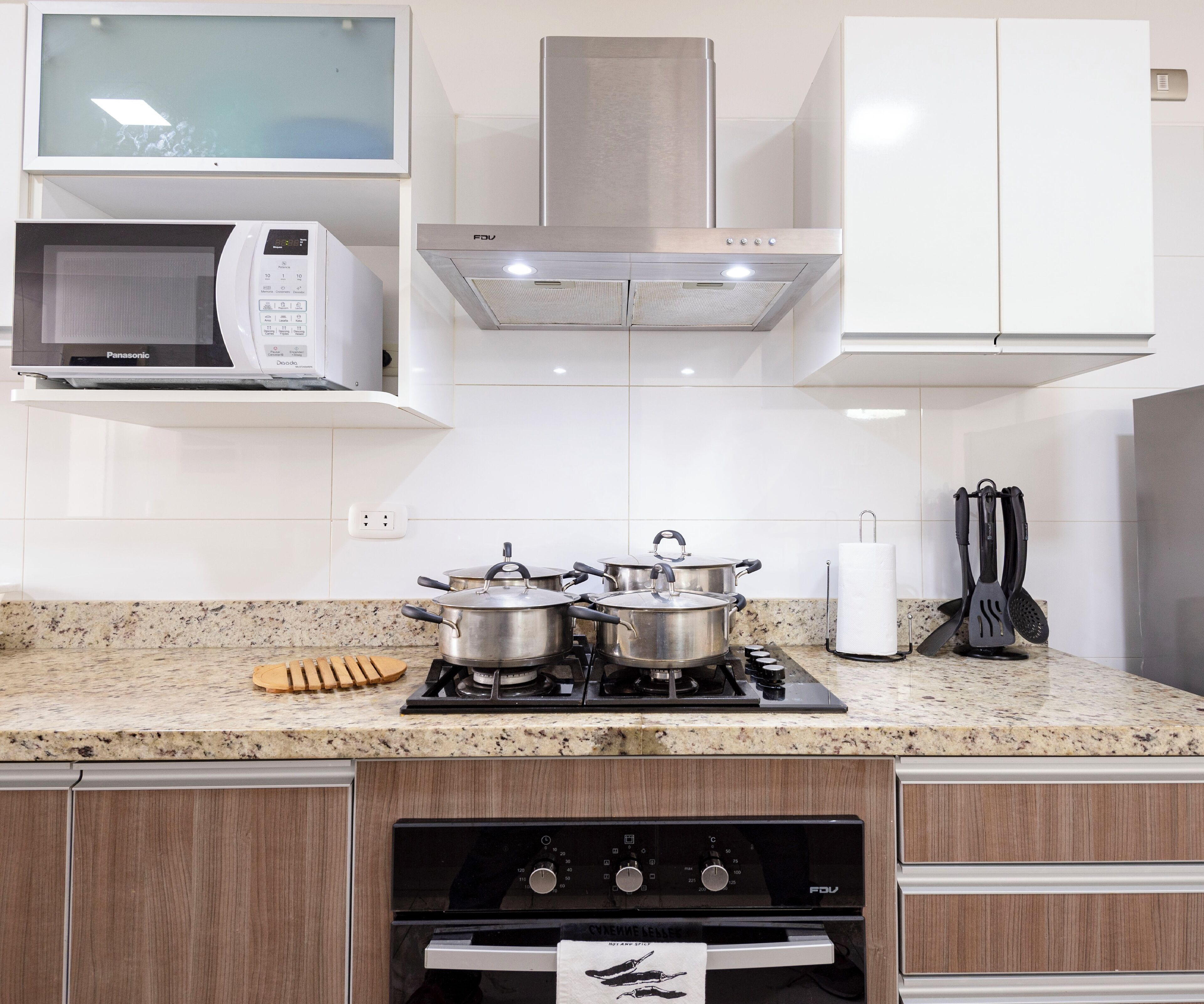 A modern kitchen with a microwave, stove, pots, and a wooden cutting board.