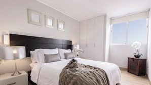 Une chambre moderne avec un grand lit, des lampes de chevet, une table de chevet, une commode et une fenêtre donnant sur un beau paysage.