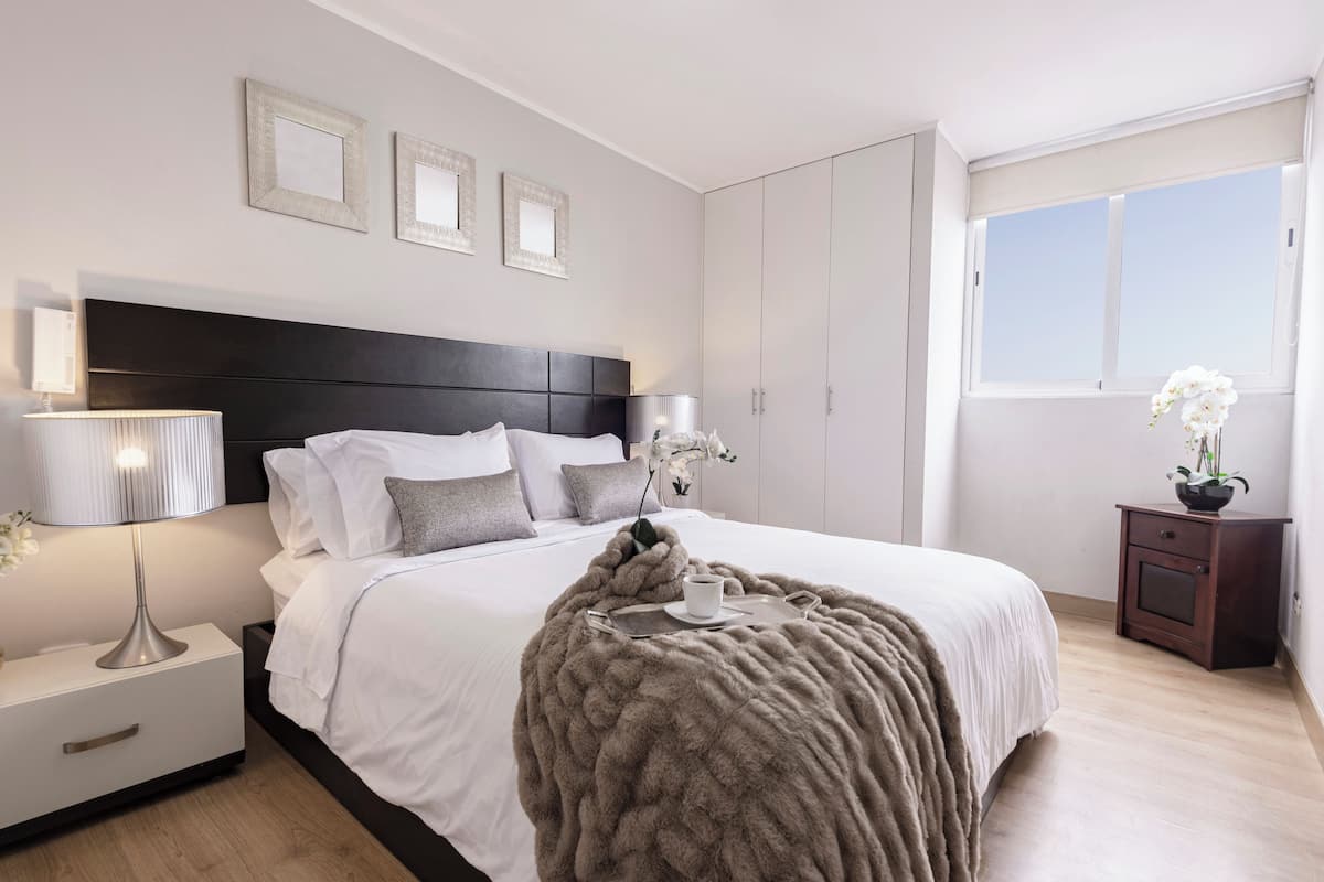 Quarto moderno com uma cama grande, luminárias de cabeceira, mesa de cabeceira, cômoda e uma janela com vista.