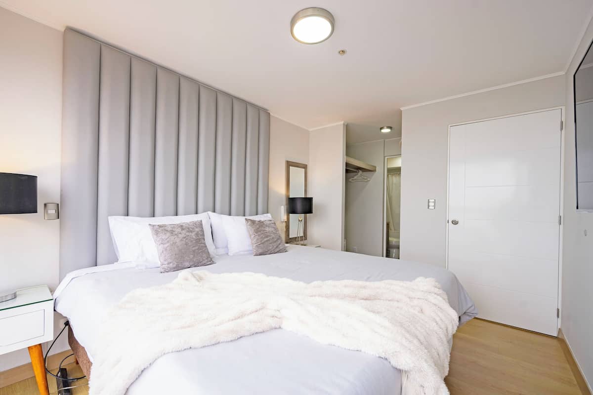 Um quarto moderno com uma cama grande, uma mesa de cabeceira, um abajur e um guarda-roupa.