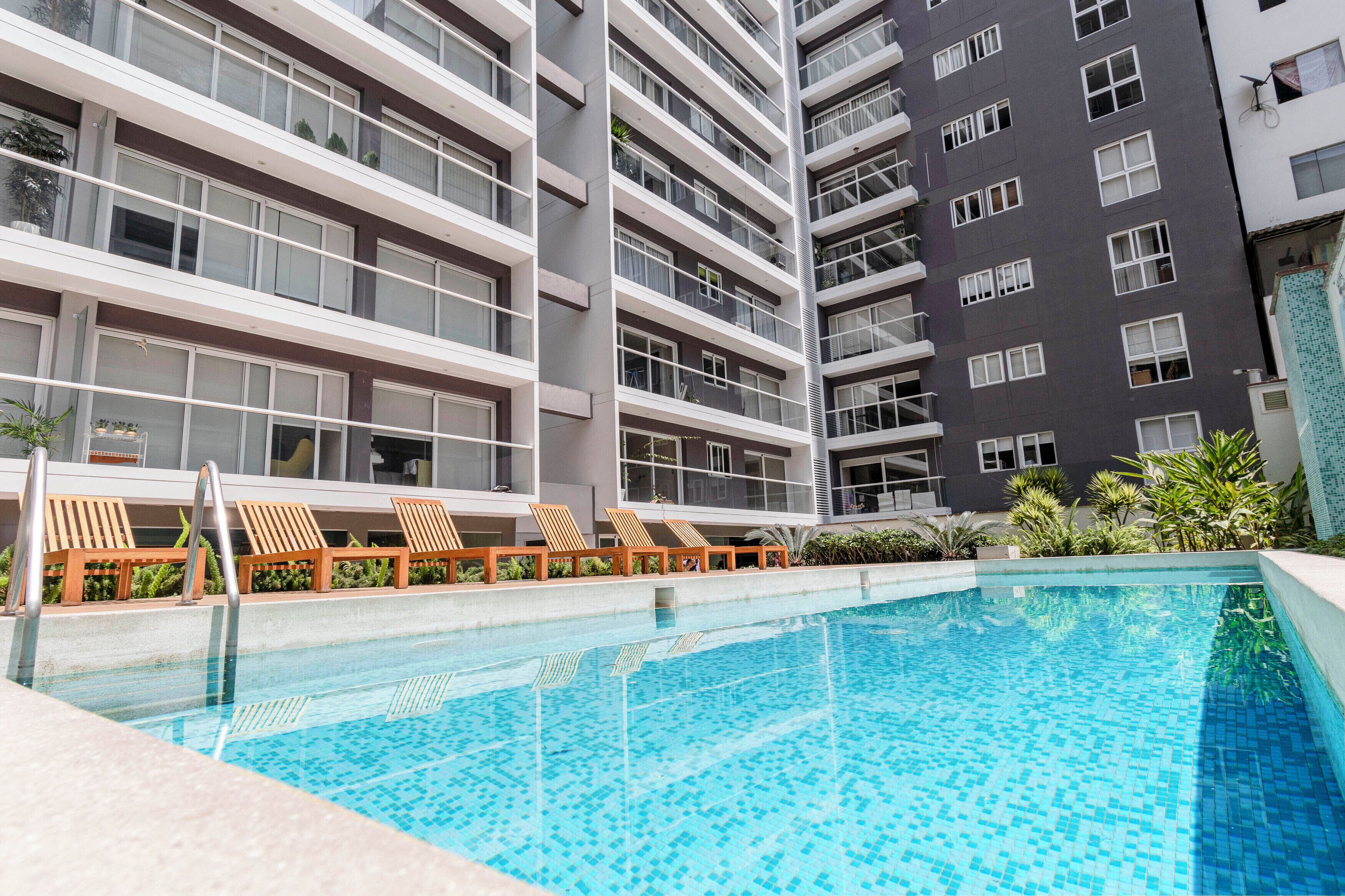 A modern hotel with a swimming pool, multiple balconies, and outdoor seating areas.
