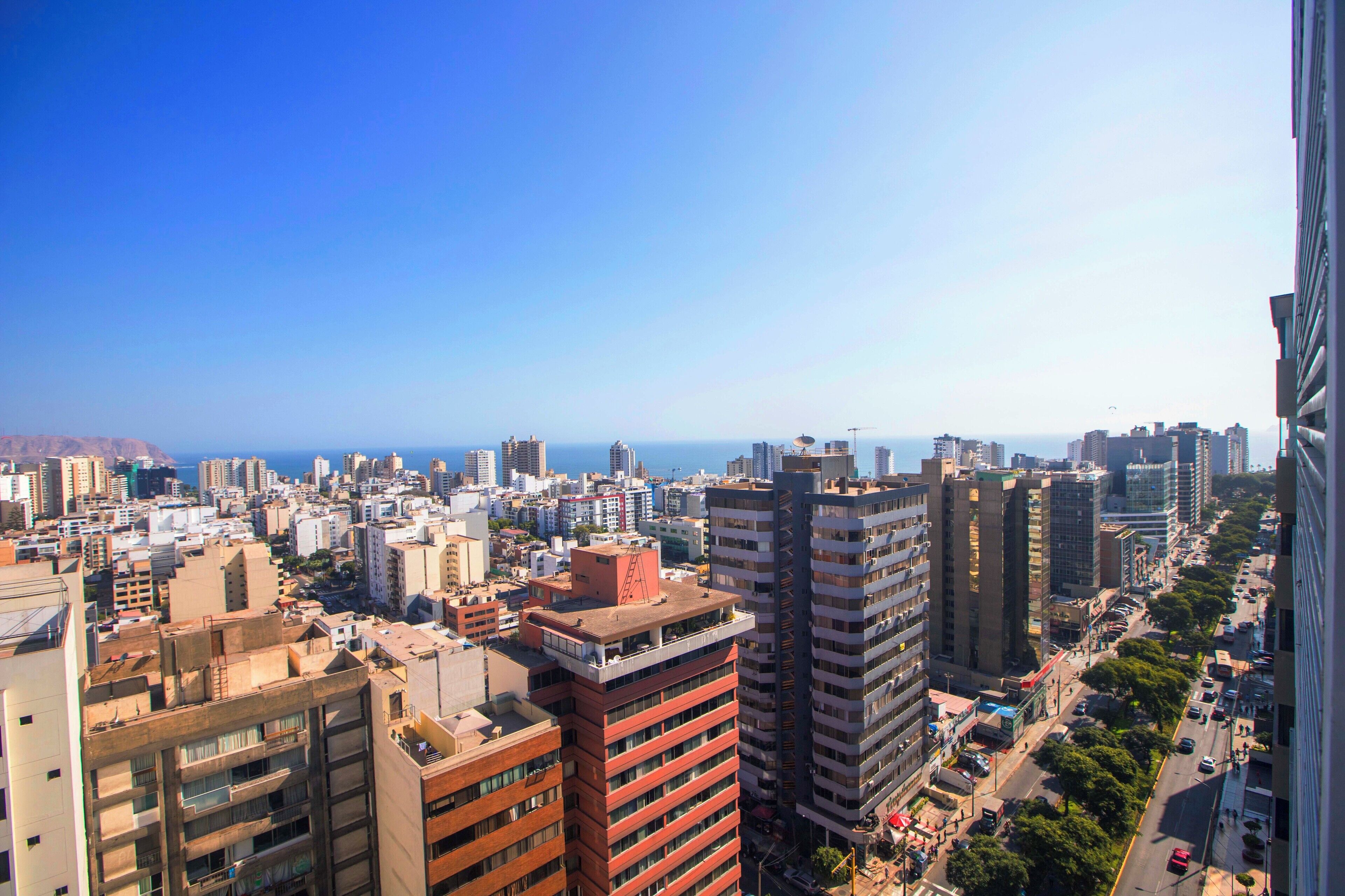Un paisaje urbano con rascacielos, cielo despejado y una vista distante del mar.