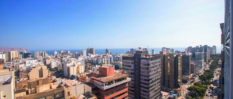 Un paisaje urbano con rascacielos, cielo despejado y una vista distante del mar.