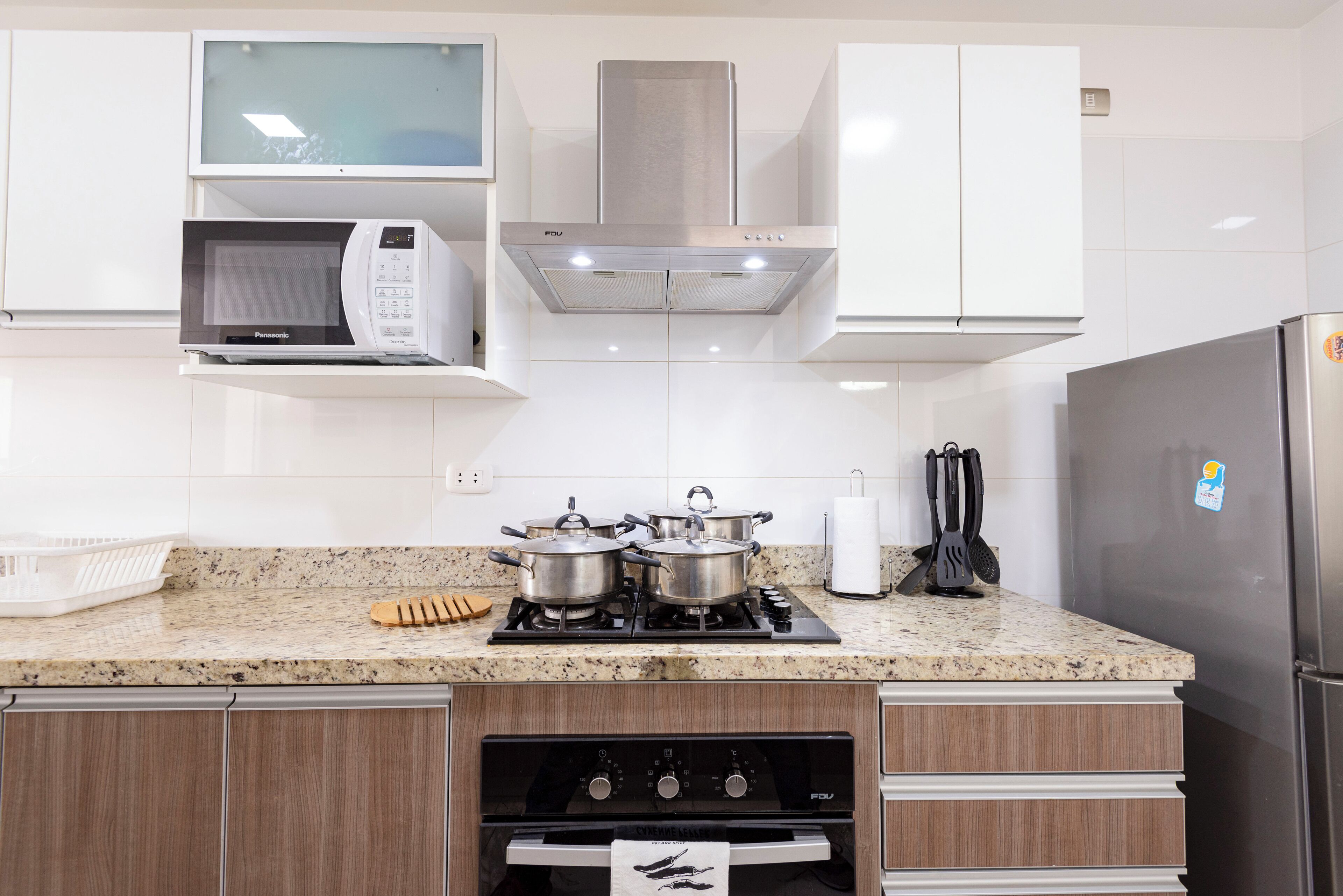 A modern kitchen with white cabinets, a microwave, a stove, and a refrigerator.