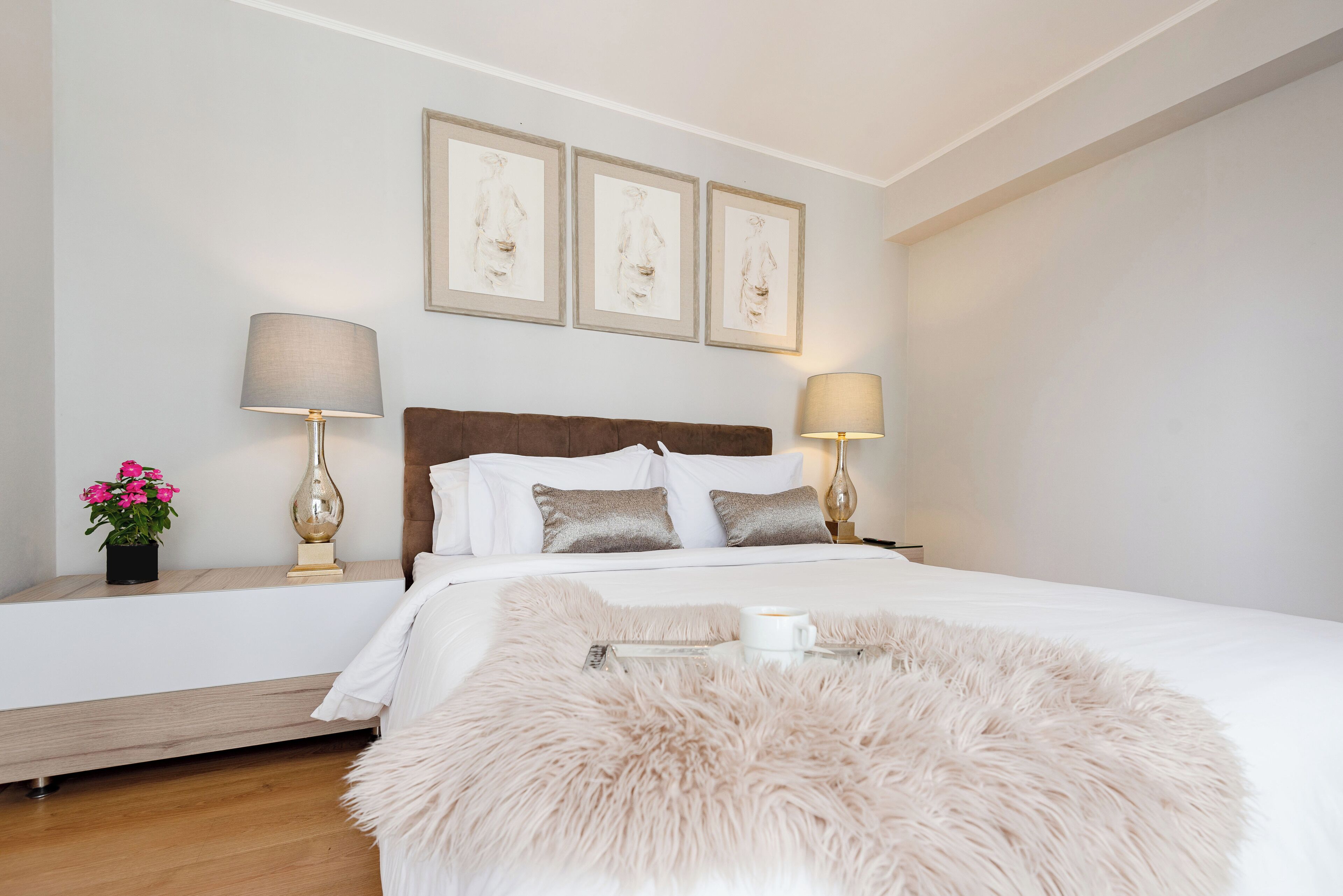 A neatly arranged bedroom with a large bed, two bedside lamps, a fluffy rug, and framed artwork on the wall.