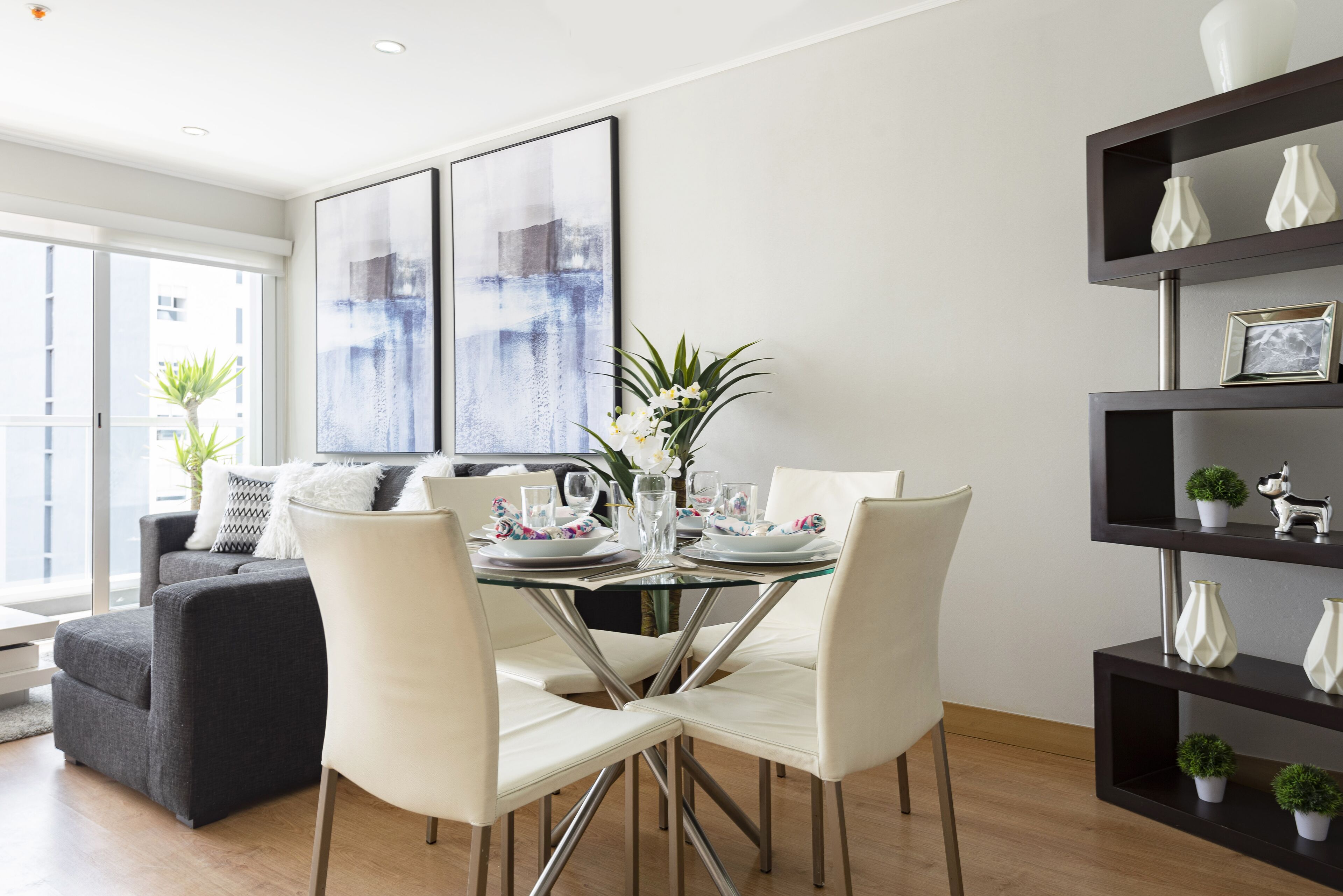 A modern dining area with a glass table, white chairs, and a dark bookshelf with decorative items.