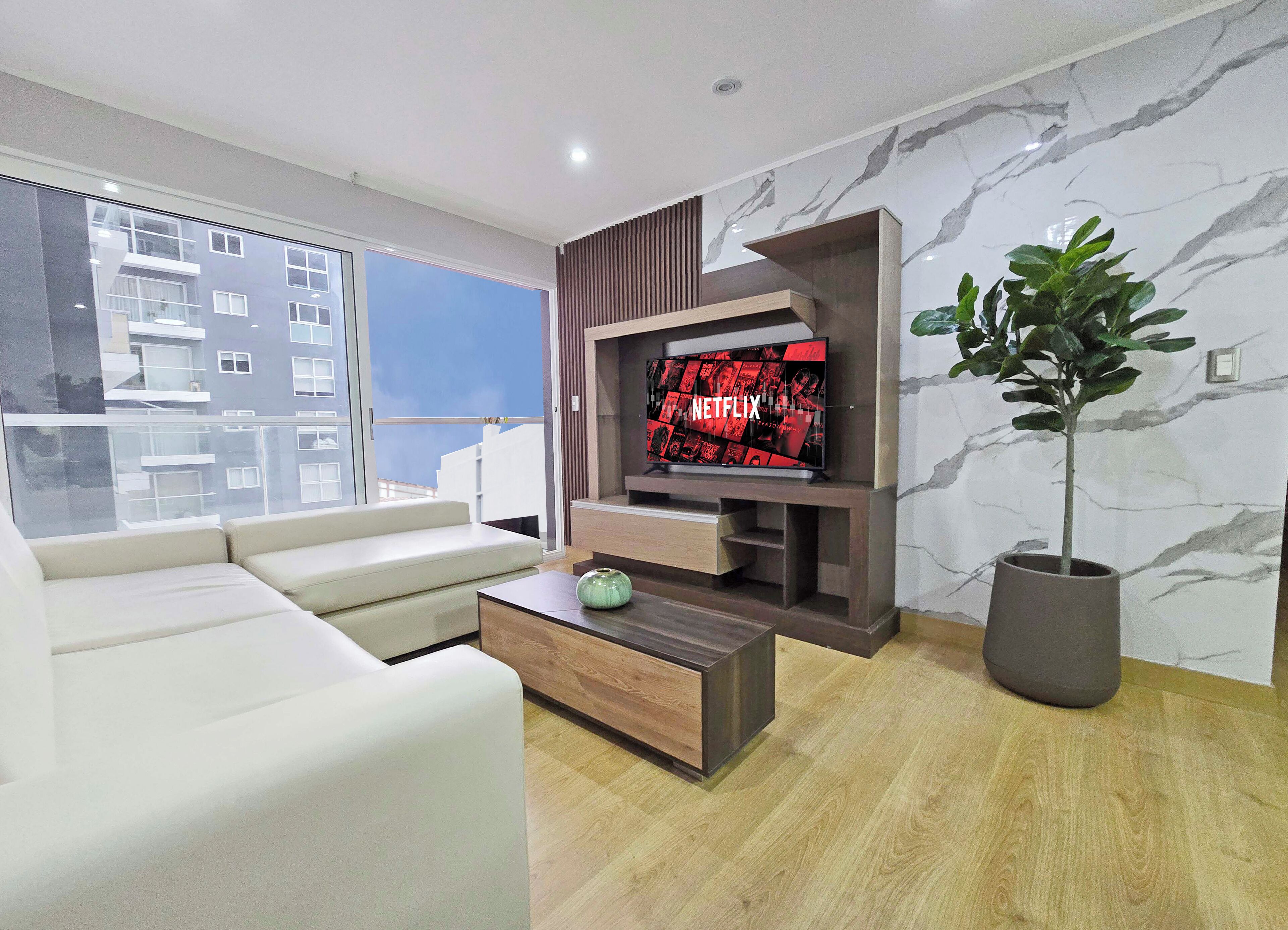Een moderne woonkamer met een flatscreen televisie, een bank, een salontafel en een potplant.